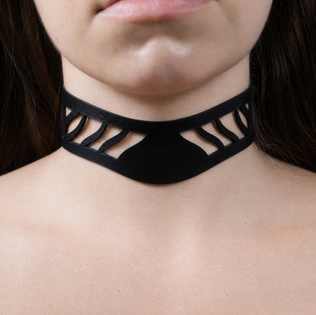 A close-up of a person's neck and chin area wearing a black choker necklace with a unique cutout design.