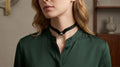 A woman wearing a green blouse with a black choker necklace and a silver ring on the chain.