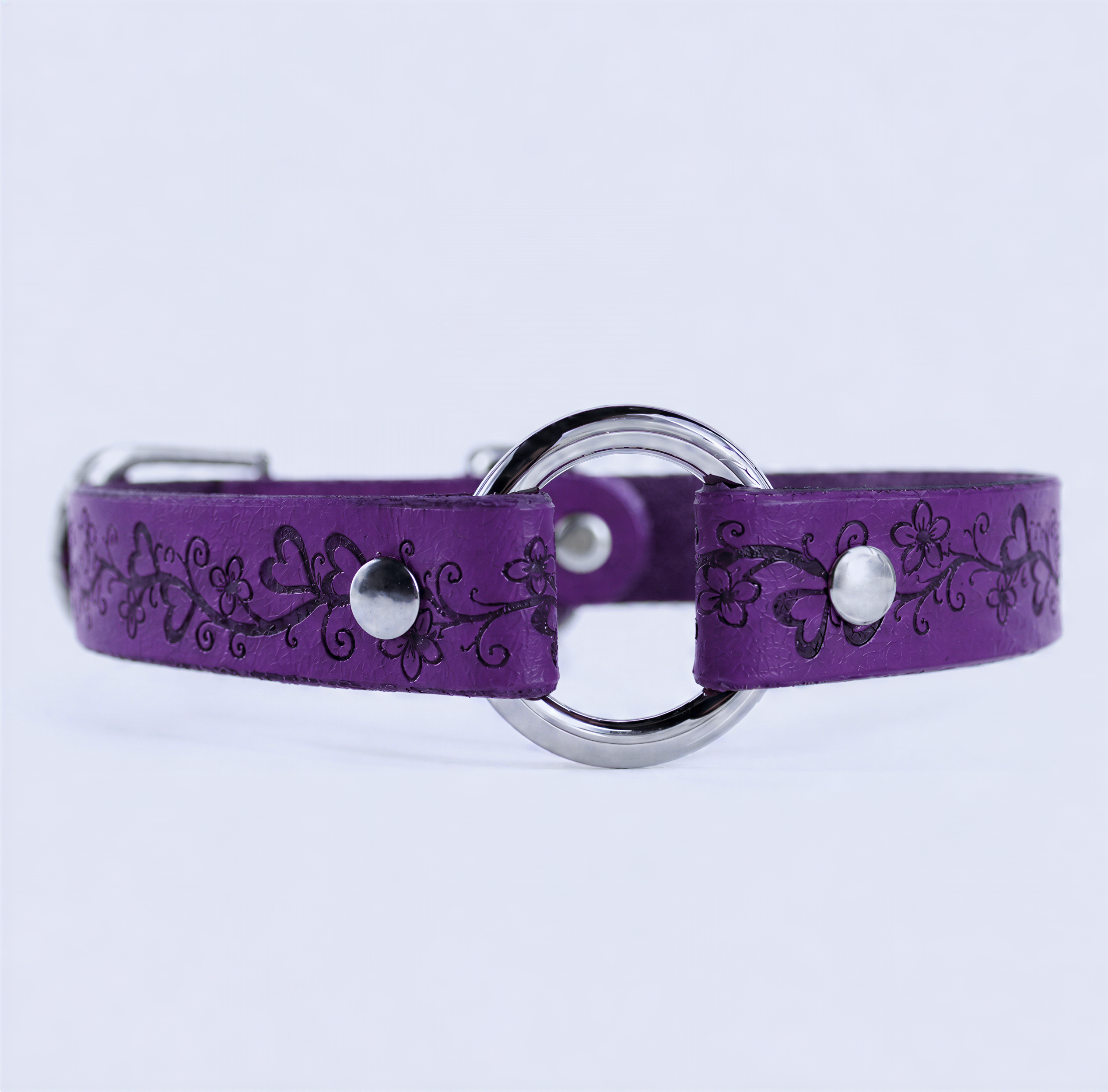 A purple leather collar with a silver metal ring and floral designs.