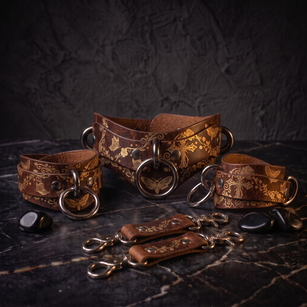 a collection of leather straps and accessories, including a corset-style belt and several leather straps with metal rings and buckles, all arranged on a dark surface.