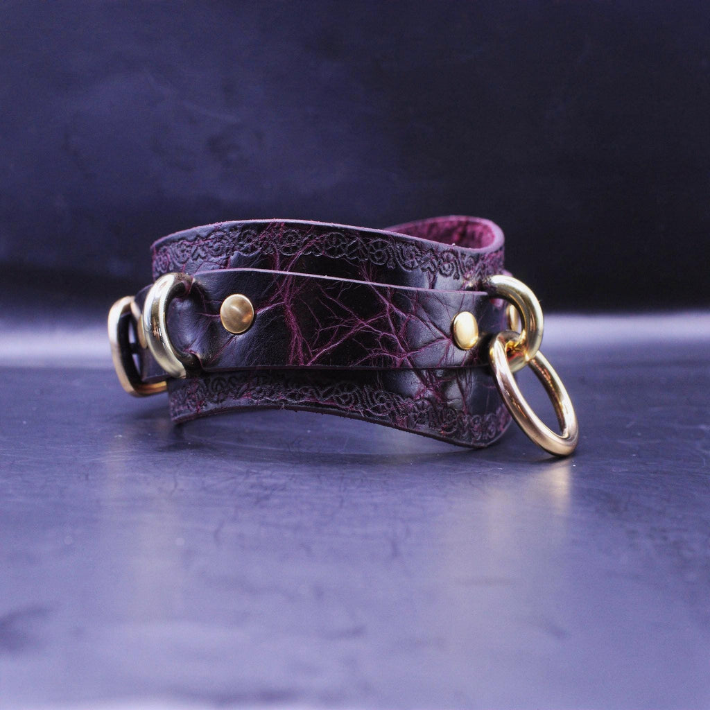 A dark purple leather choker necklace with gold-colored metal rings and a decorative pattern on the clasp.