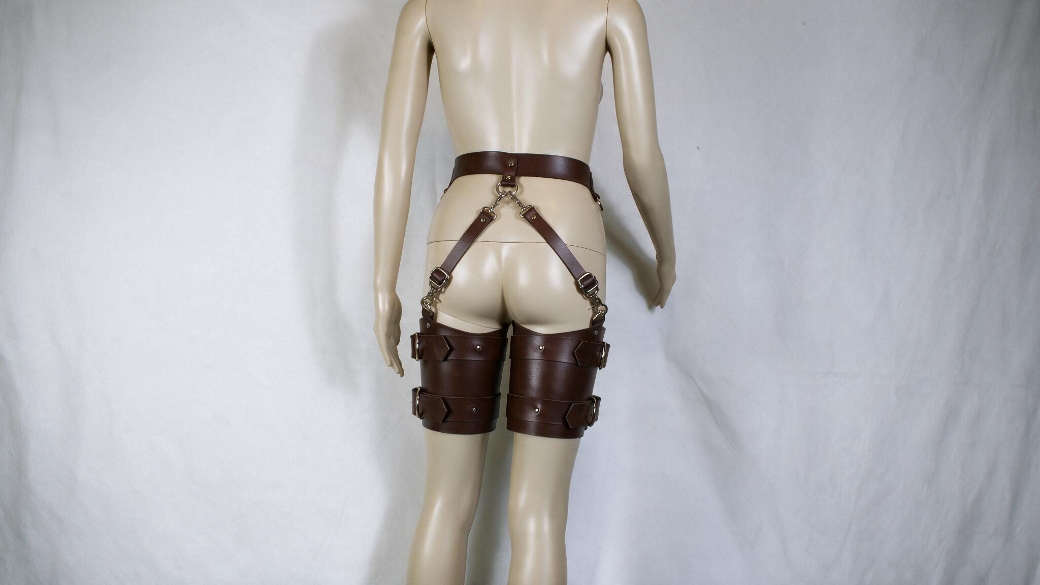 A mannequin wearing a pair of brown leather garter belts and garter straps.