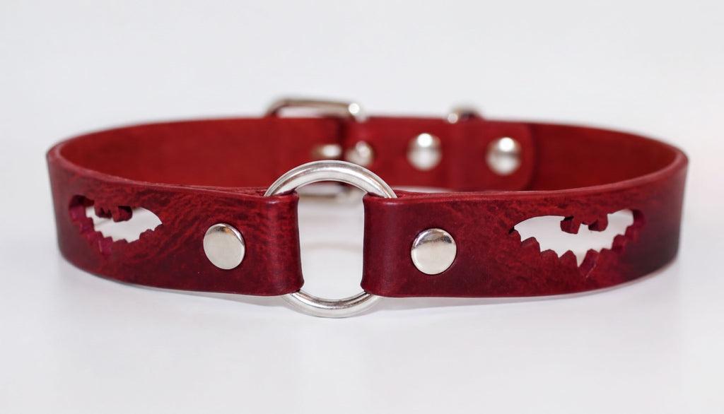 A red leather dog collar with a silver ring and cutouts of bats.