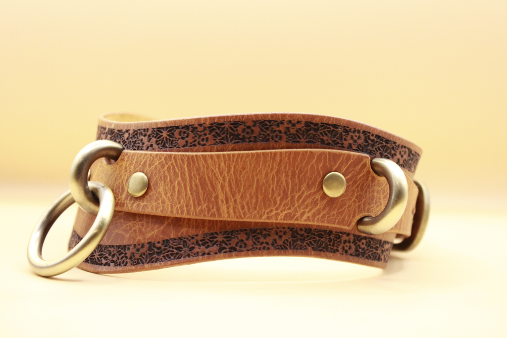 A brown leather belt with a floral pattern and metal rings, displayed against a yellow background.