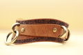A brown leather belt with a floral pattern and metal rings, displayed against a yellow background.