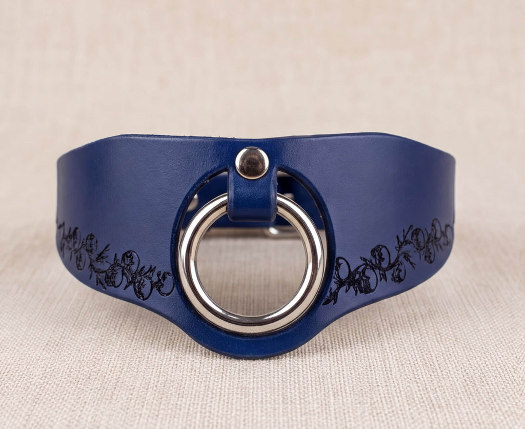 A blue leather choker necklace with a silver ring and floral design on the side.