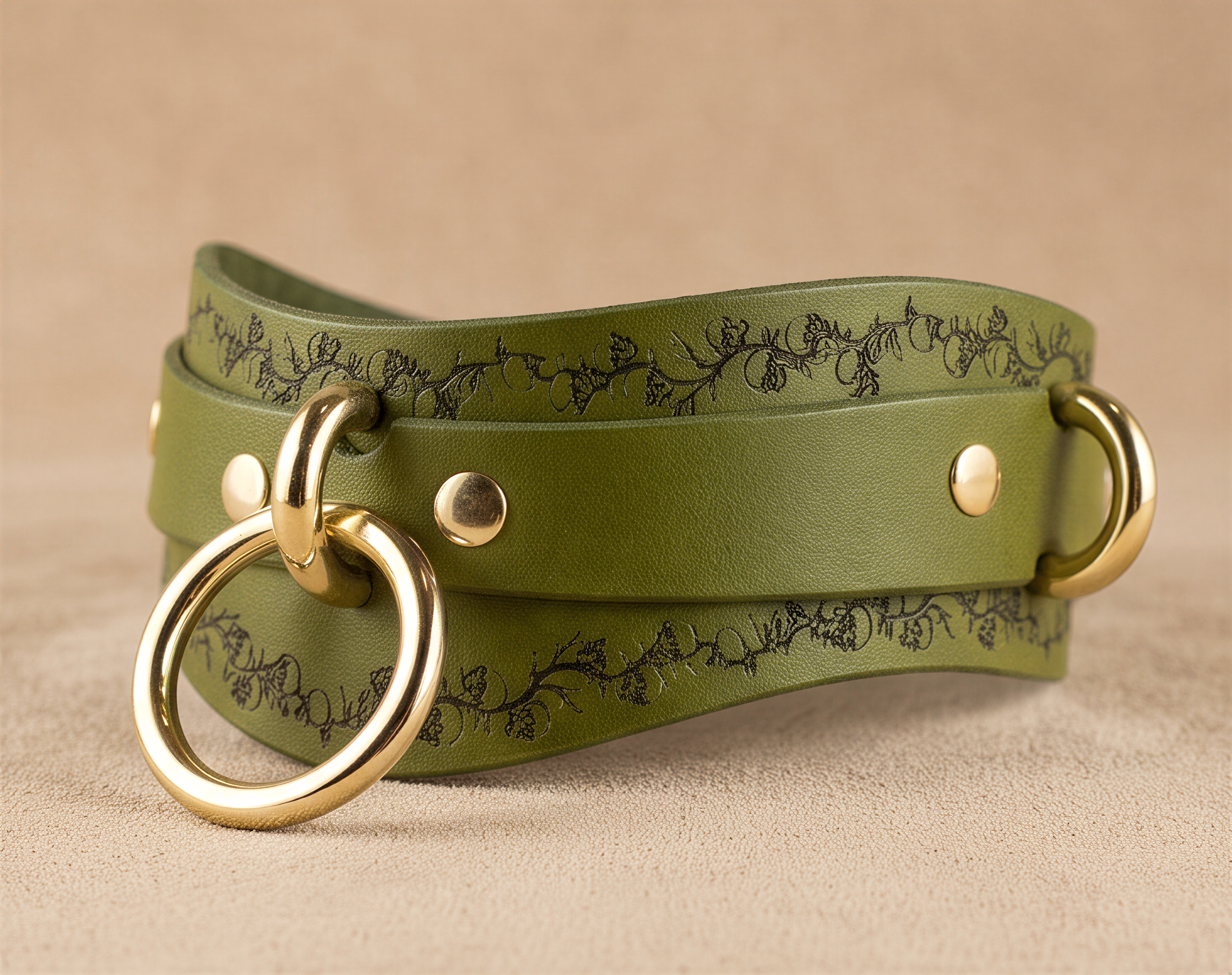 A green leather belt with a decorative floral pattern and two gold-colored metal rings on the front.