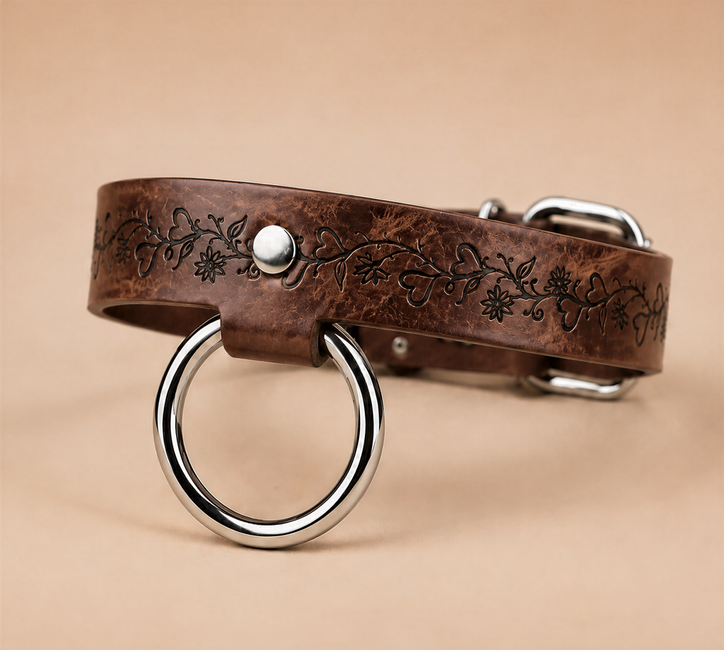 A brown leather dog collar with a metal ring and a decorative floral pattern on the band.