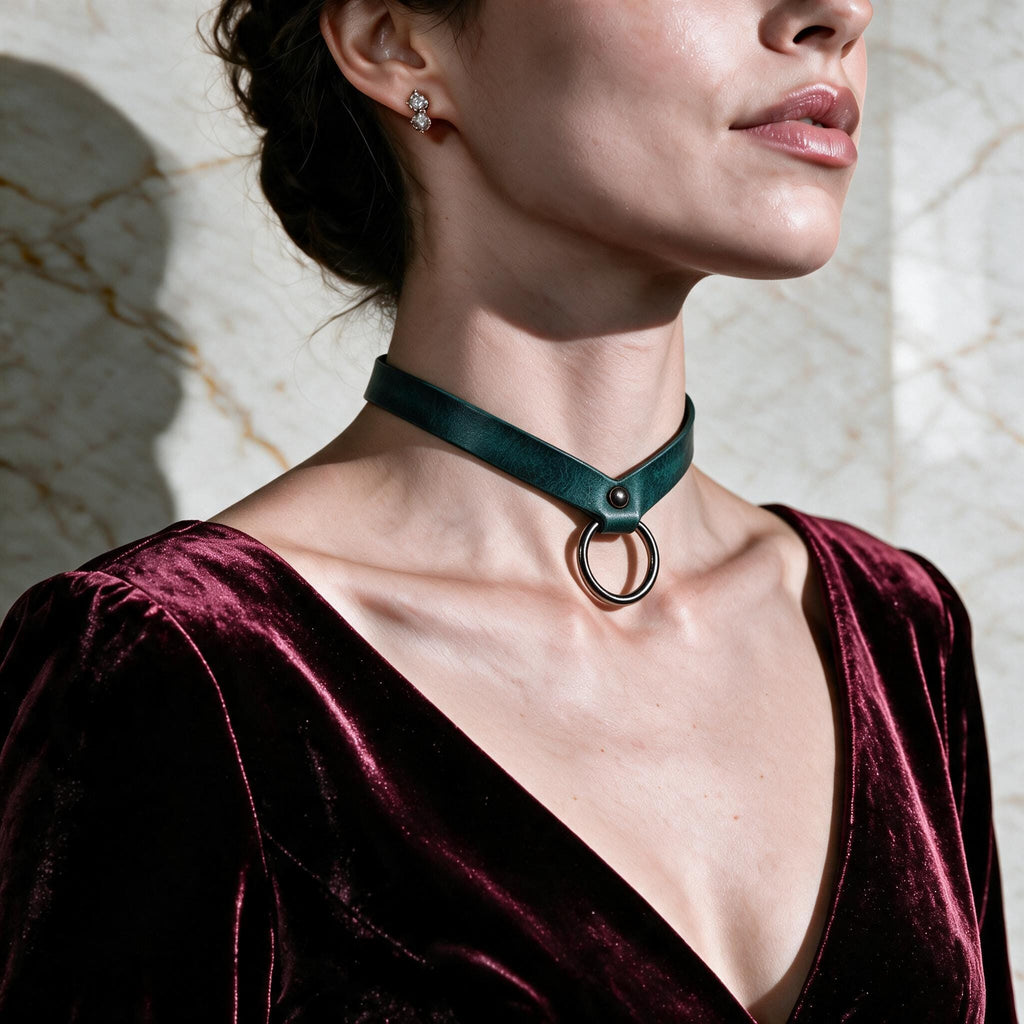 A woman wearing a green choker necklace with a circular ring on it, standing against a marble wall.