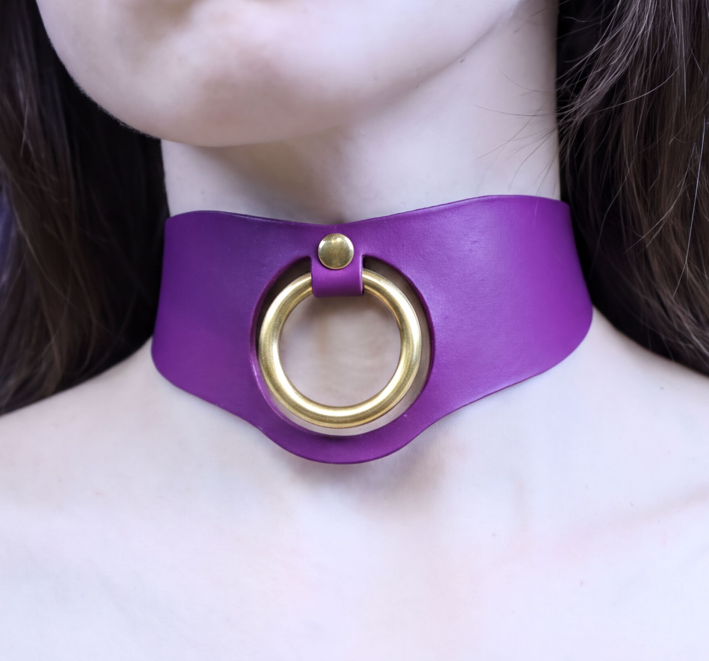 A close-up of a person's neck wearing a purple choker necklace with a gold ring.
