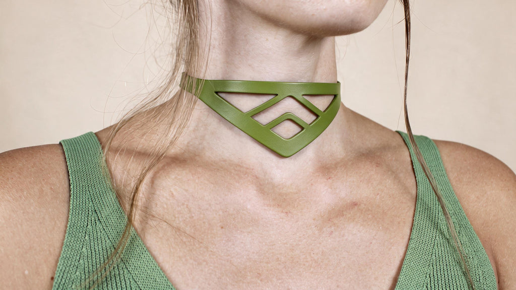 A close-up of a woman wearing a green choker necklace with a geometric pattern.