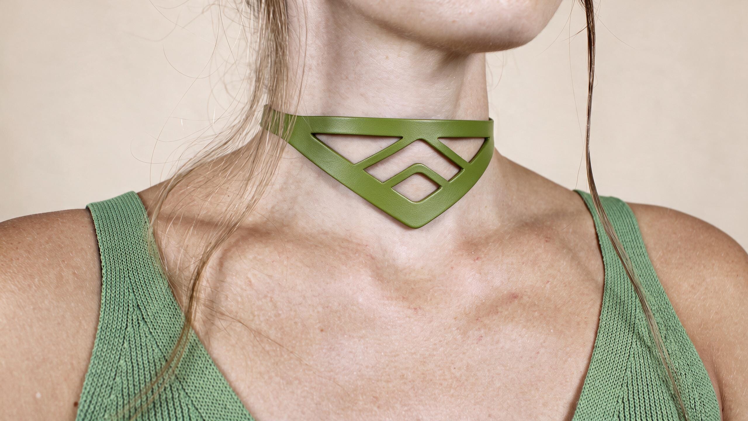 A close-up of a woman wearing a green choker necklace with a geometric pattern.