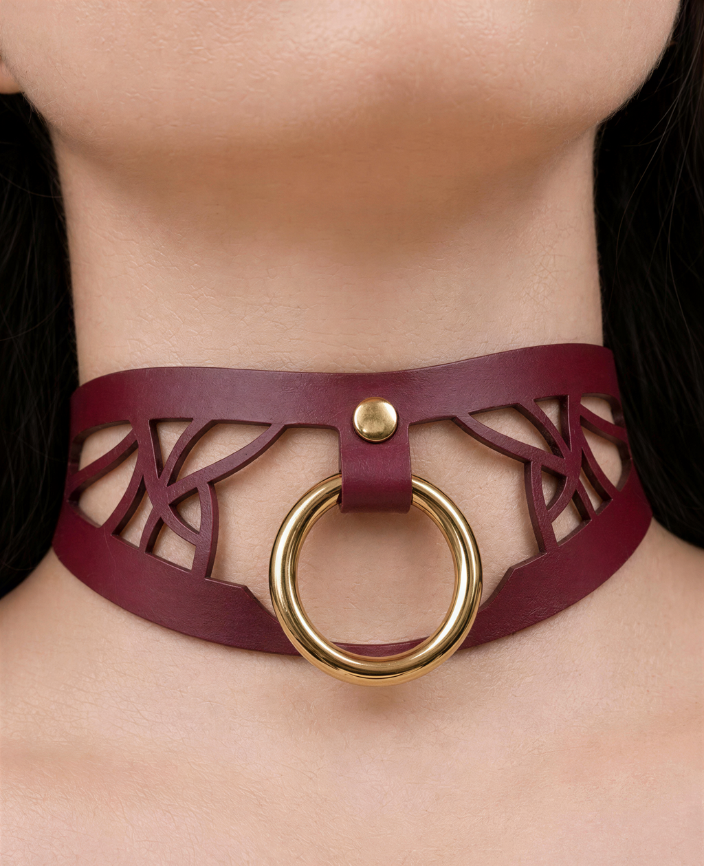 A close-up view of a woman's neck and chest area wearing a burgundy choker necklace with a gold ring.