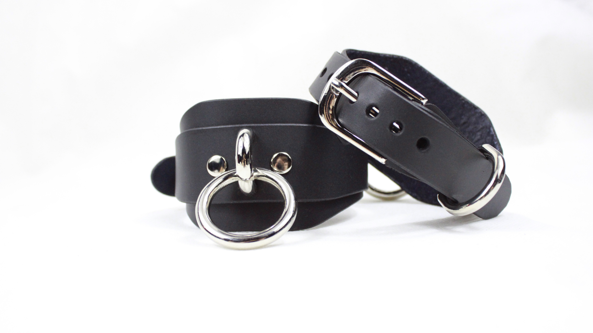 A pair of black leather straps with metal rings and buckles, placed on a white background.