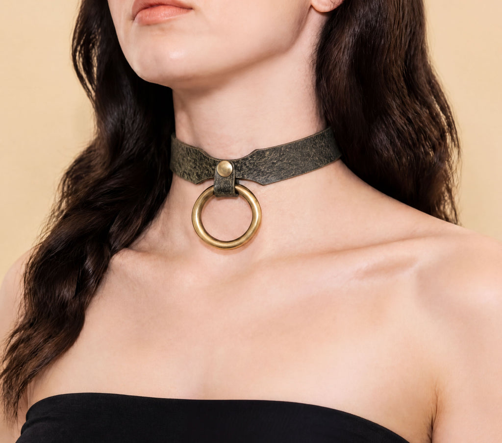 A woman wearing a green choker necklace with a gold ring on it.