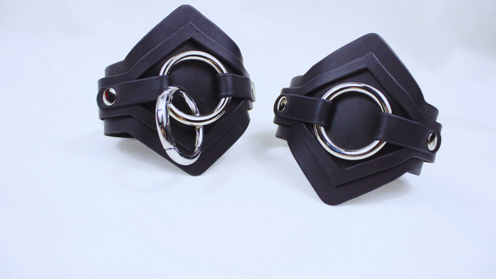 two black leather cuffs with metal rings on them, placed side by side on a white background.
