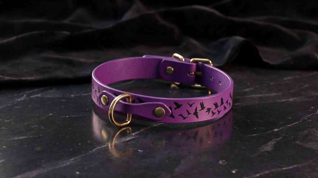 A purple leather collar with a bird design on it, placed on a black marble surface.