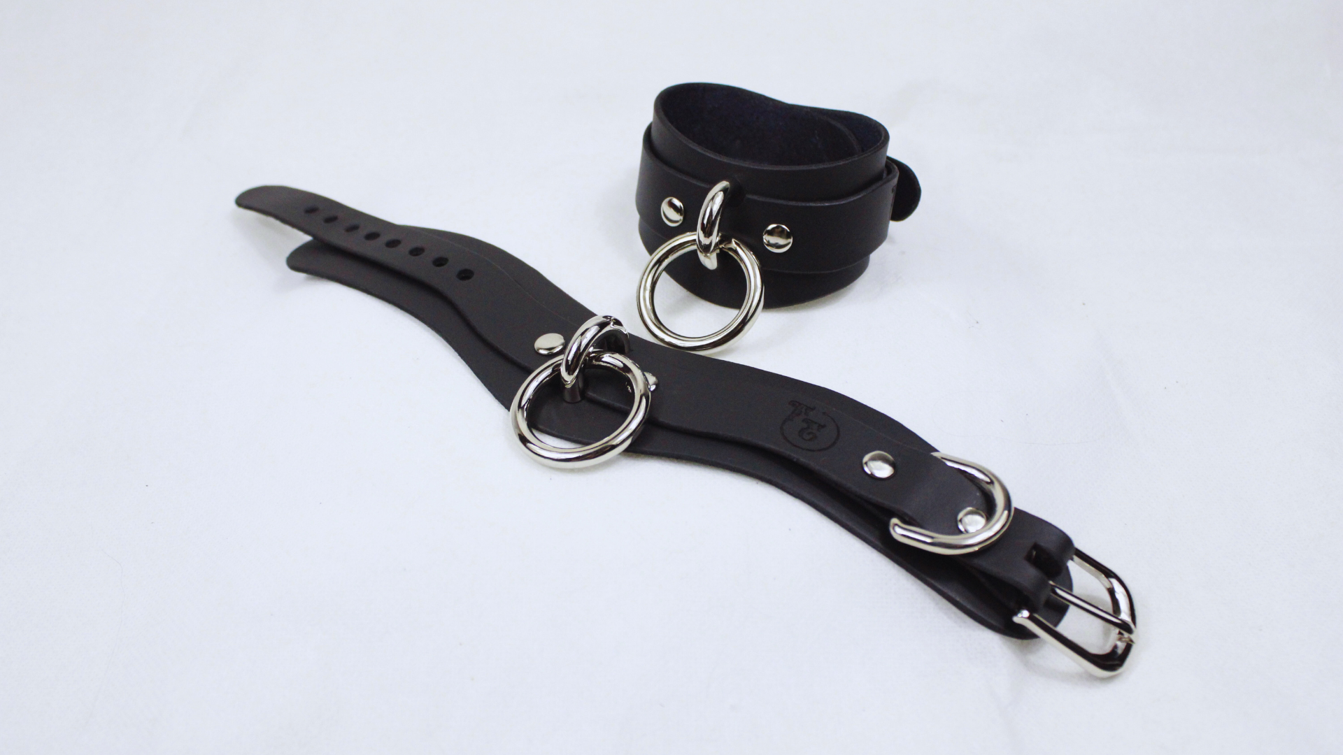 A black leather strap with metal rings and buckles, possibly used for BDSM or BDSM-related accessories.