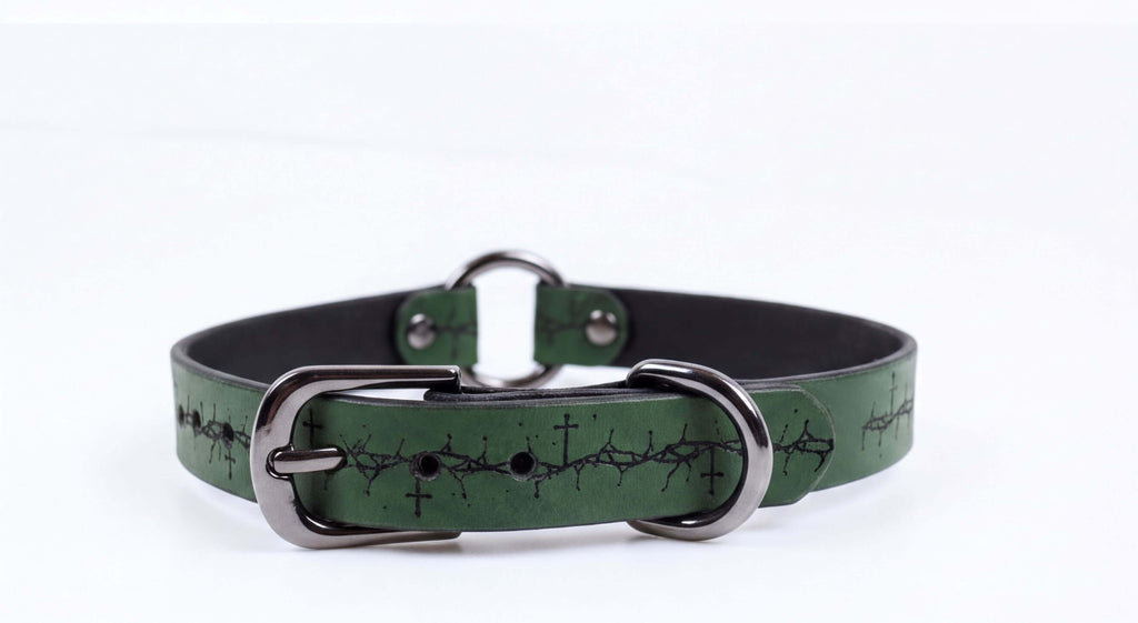 A green leather collar with a metal buckle and a design of crosses on the surface.