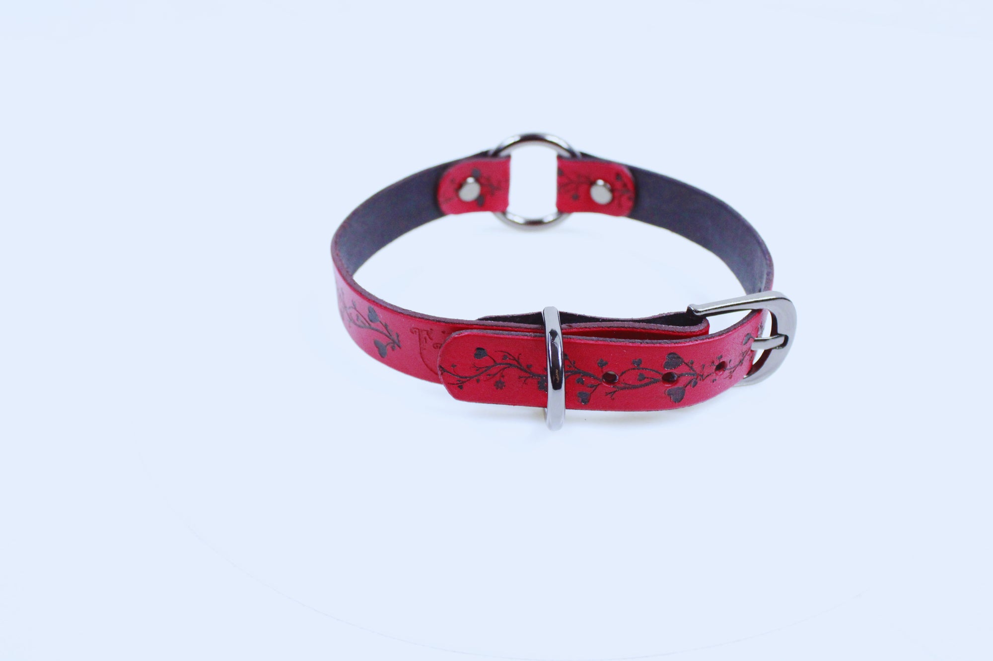 A red leather collar with a silver buckle and a floral pattern on the strap.