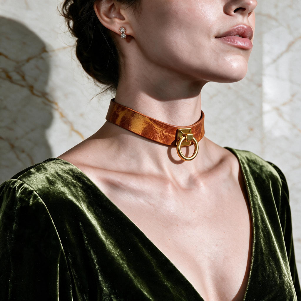 A woman wearing a green velvet dress with a gold choker necklace and earrings, posing against a marble wall.