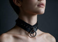 A close-up of a person's neck and chest area wearing a black leather choker necklace with a metal ring.