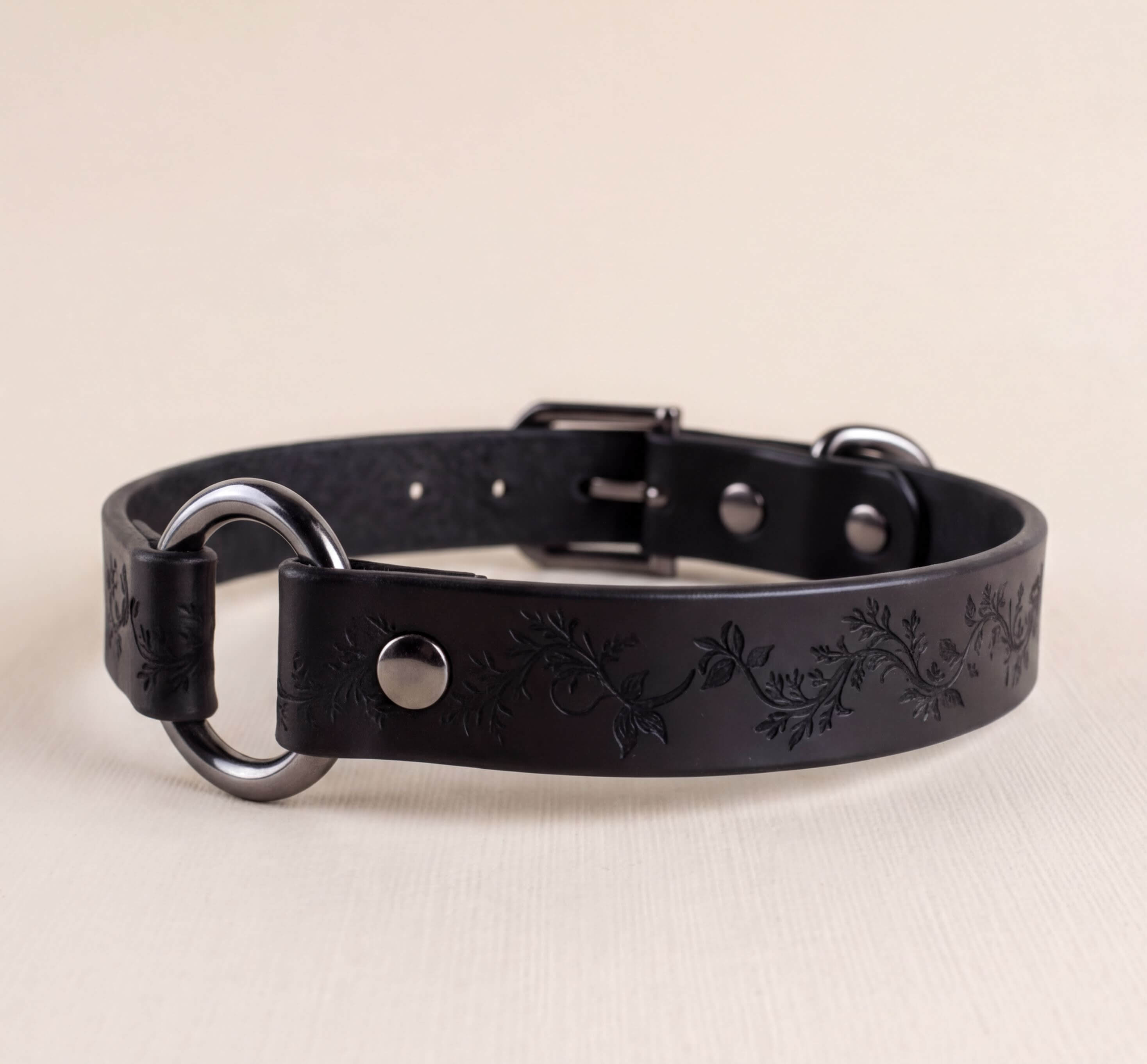 A black leather collar with a metal ring and decorative leaf pattern.