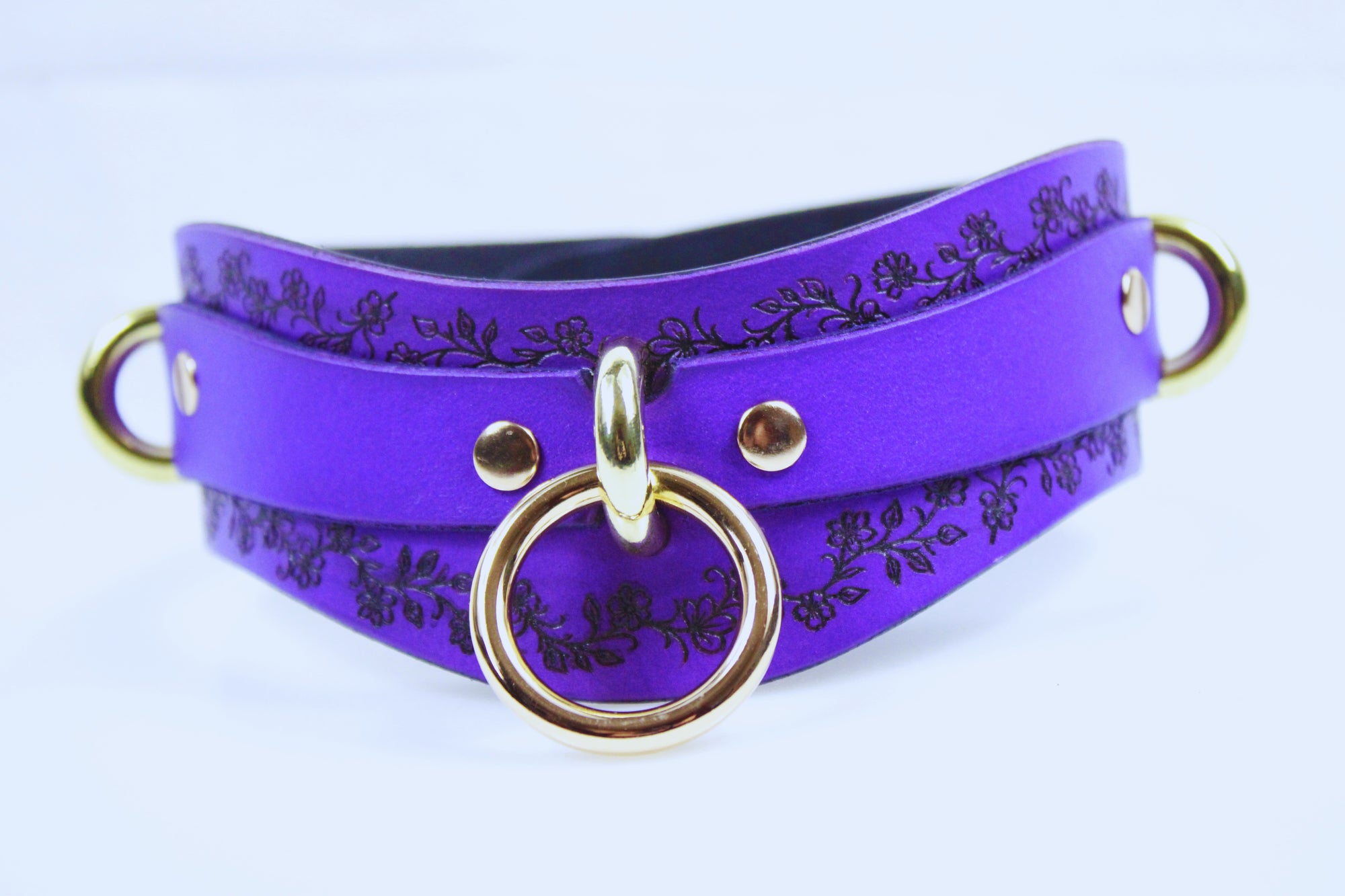 A purple leather choker necklace with a gold-colored ring and two gold-colored rings on either side.