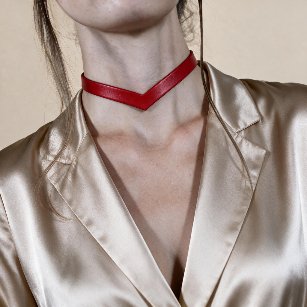 A close-up of a person wearing a red choker necklace and a beige blazer.