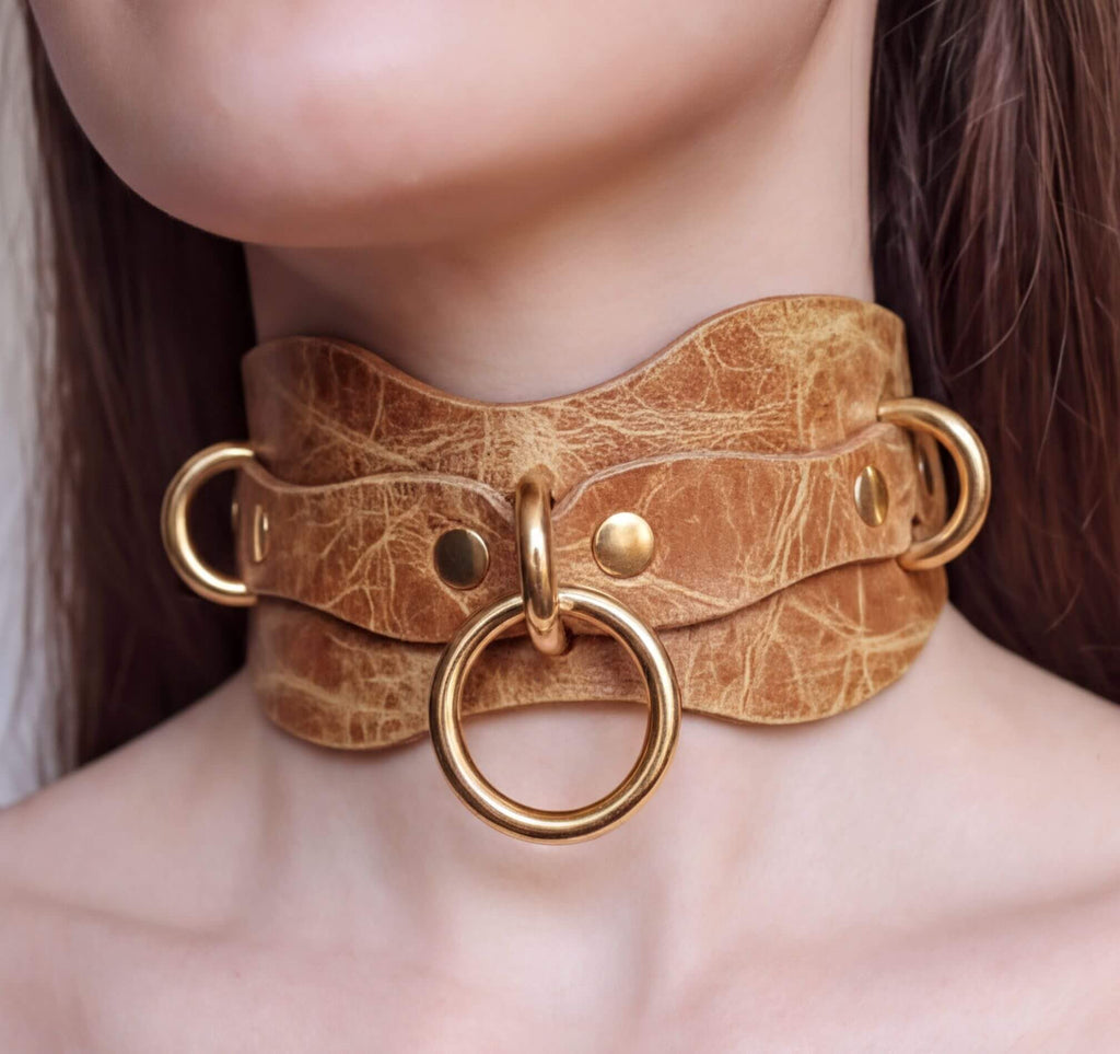 A close-up of a woman's neck wearing a choker necklace with a large gold ring and metal rings.