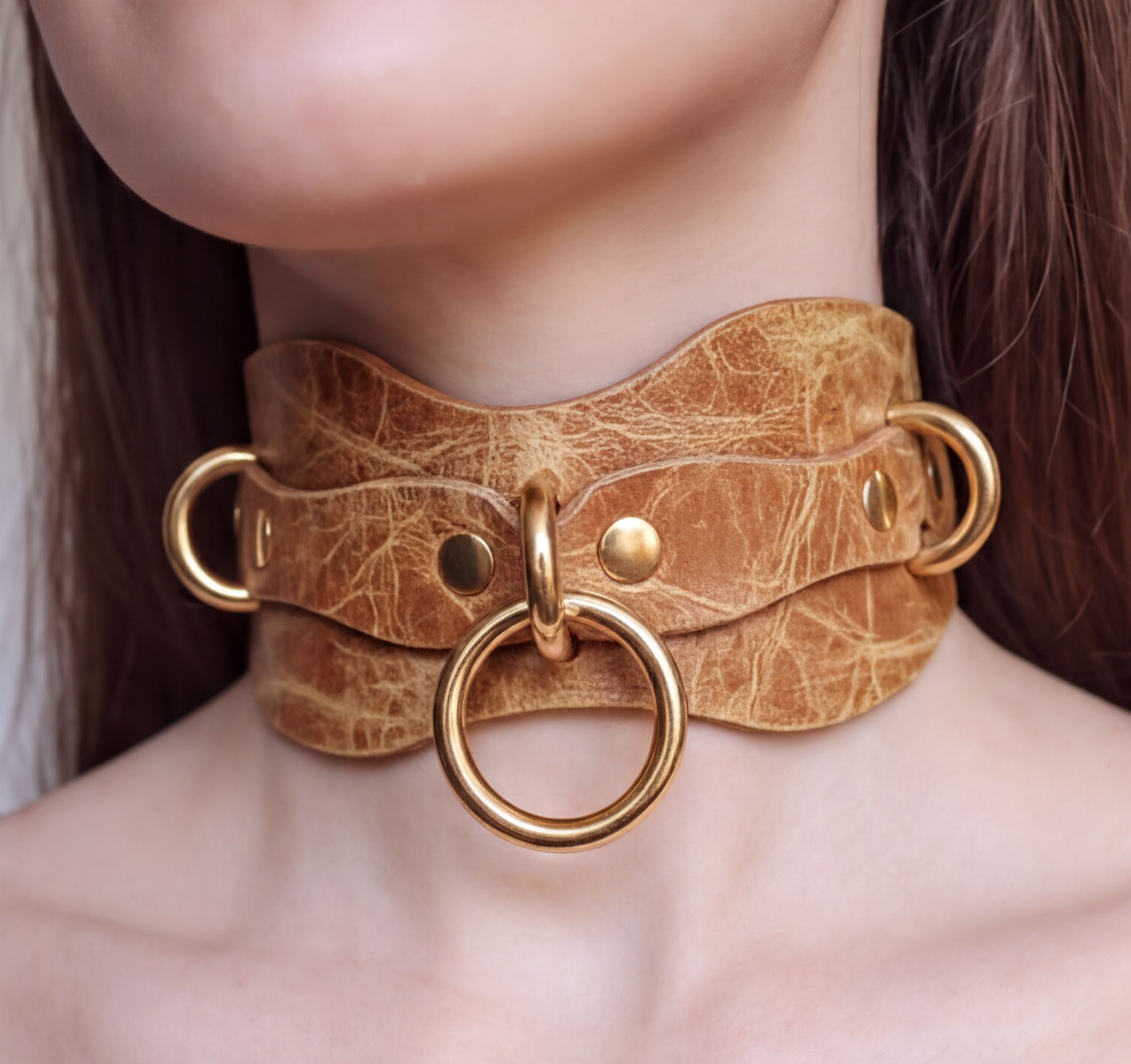A close-up of a woman's neck wearing a choker necklace with a large gold ring and metal rings.