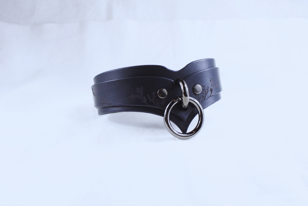 A black leather choker necklace with a metal ring and a decorative element on the front.