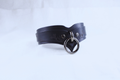 A black leather choker necklace with a metal ring and a decorative element on the front.