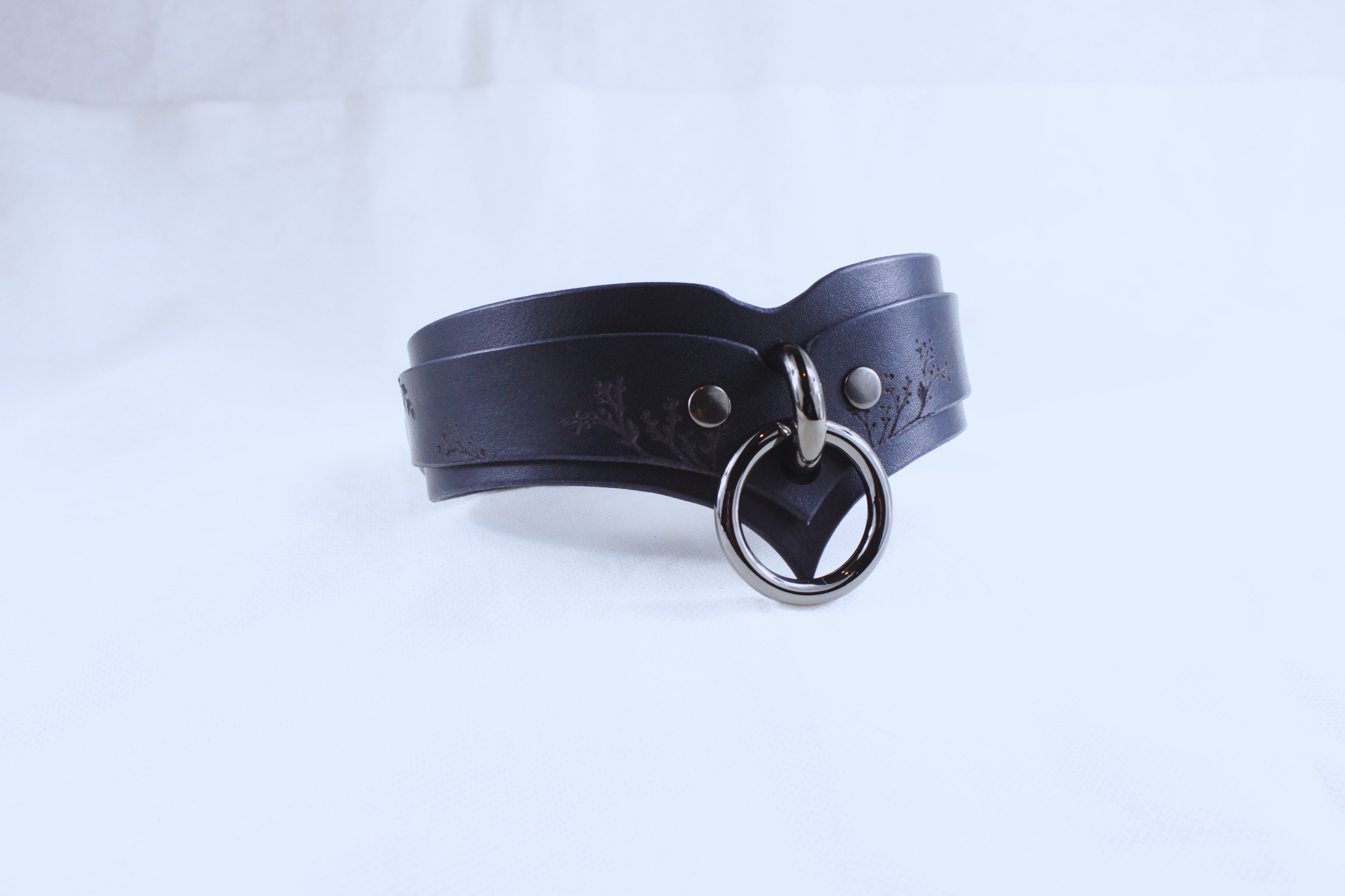 A black leather choker necklace with a metal ring and a decorative element on the front.