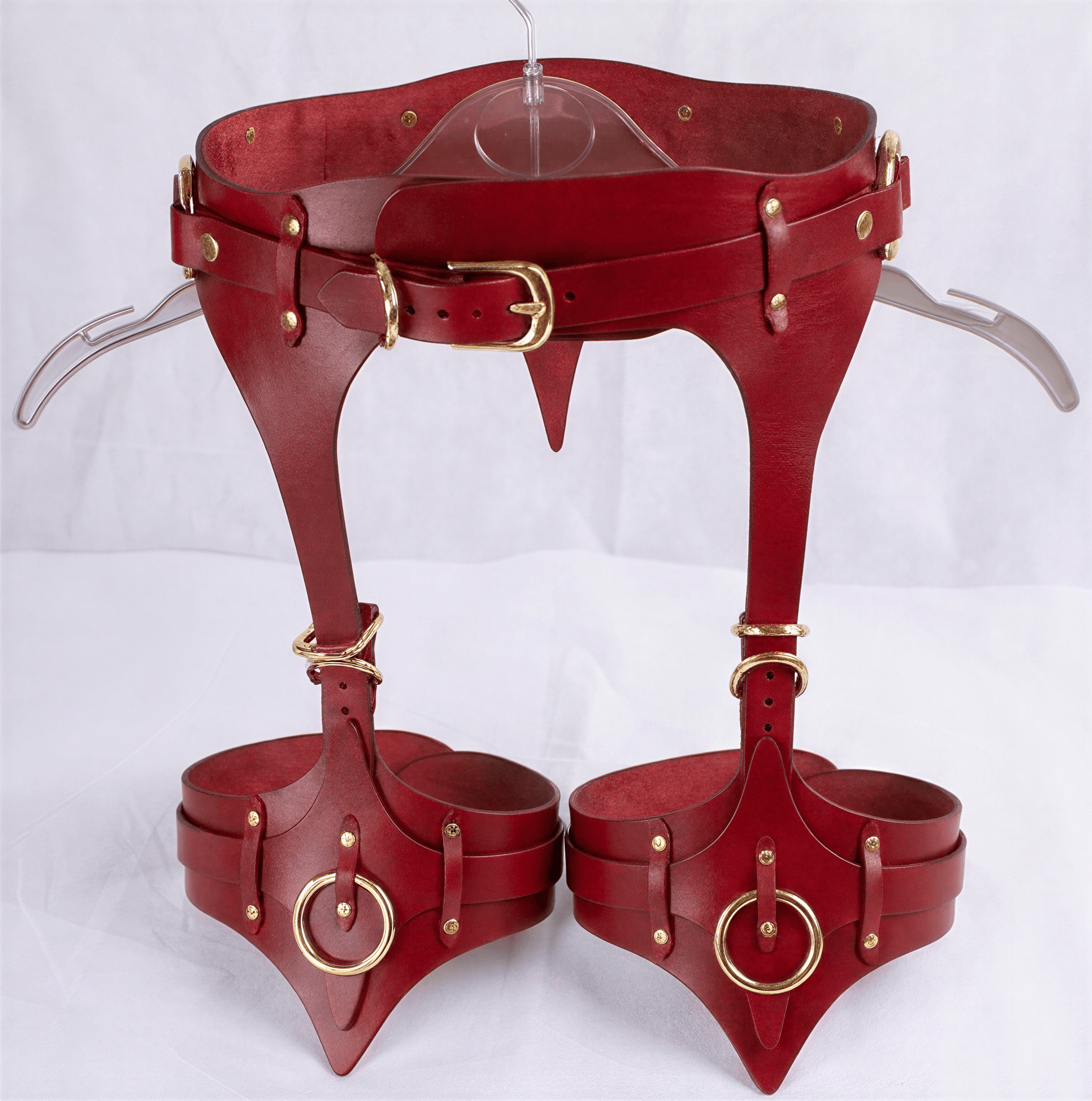 A pair of red leather corsets with metal studs and buckles, displayed on a hanger.