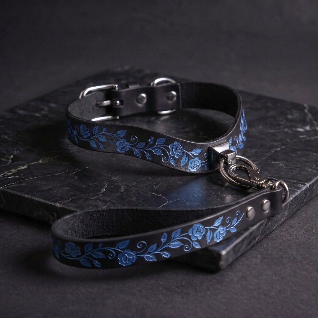 A black leather collar with blue floral designs and a matching leash are displayed on a dark surface.