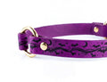 A purple leather dog collar with a black bat and star design pattern.