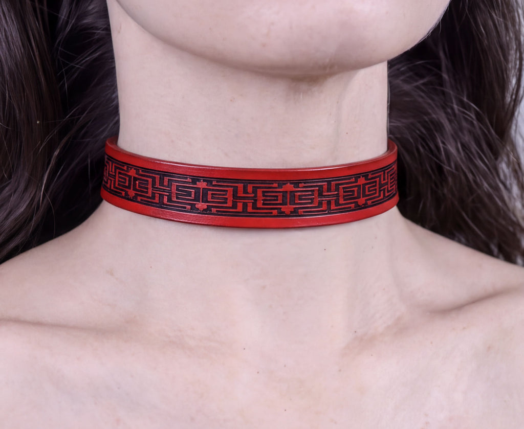 A close-up of a person's neck wearing a red choker necklace with a black geometric pattern.