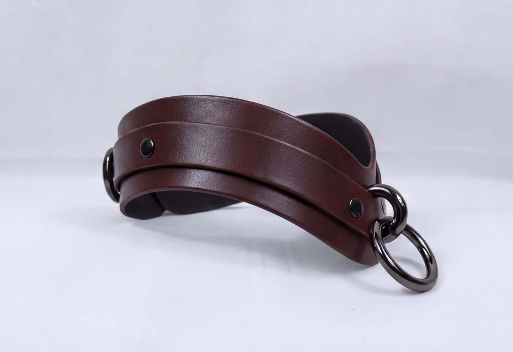 A brown leather choker necklace with metal rings and a black strap.