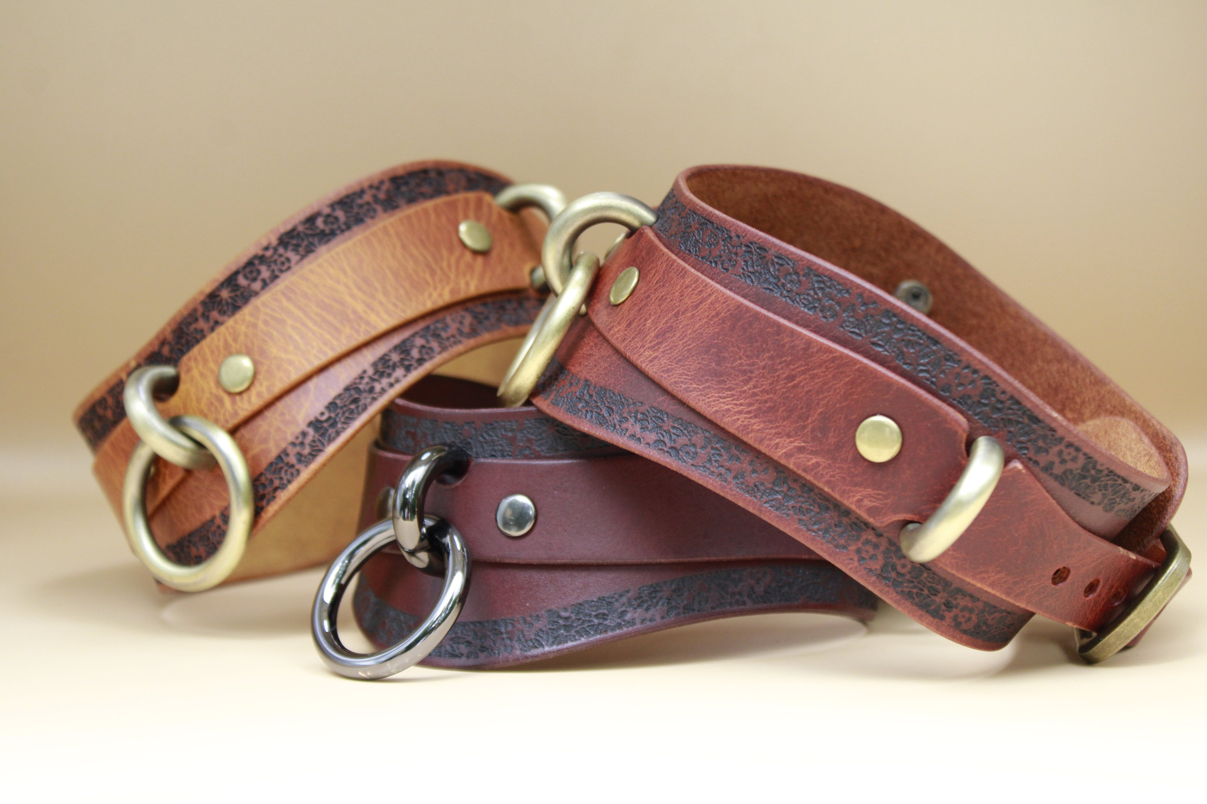 Three leather choker necklaces with metal rings and buckles are displayed on a beige background.