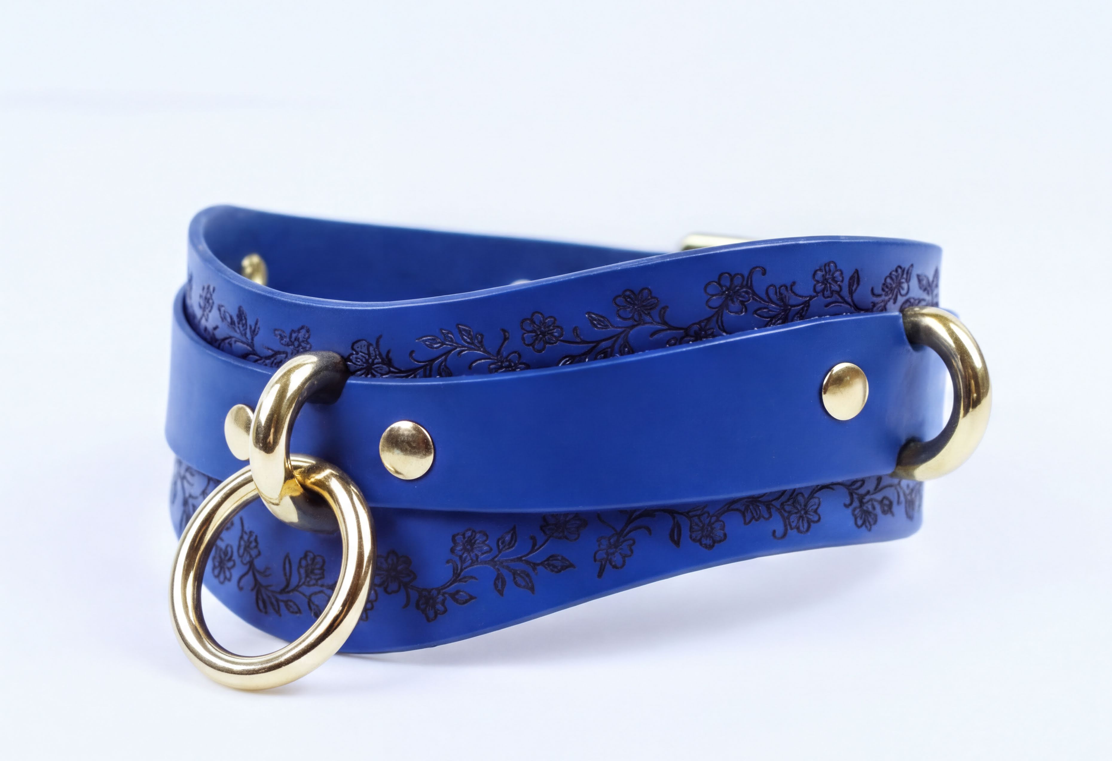 A blue leather strap with a floral pattern and two gold-colored metal rings on the ends.