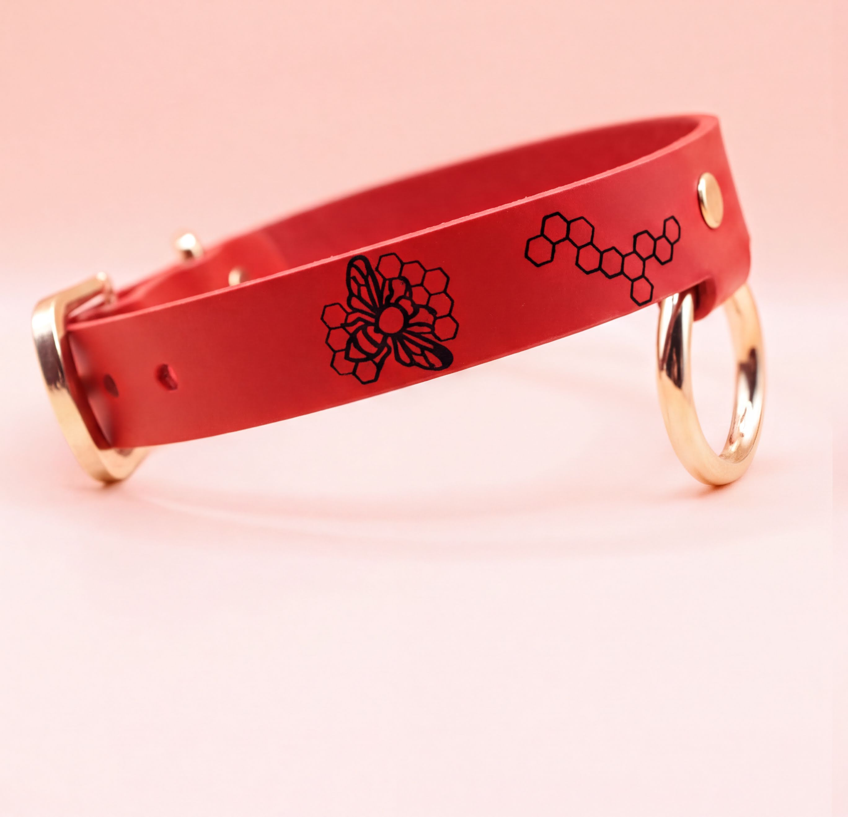 A red leather collar with a floral design and two gold-colored rings on the sides.