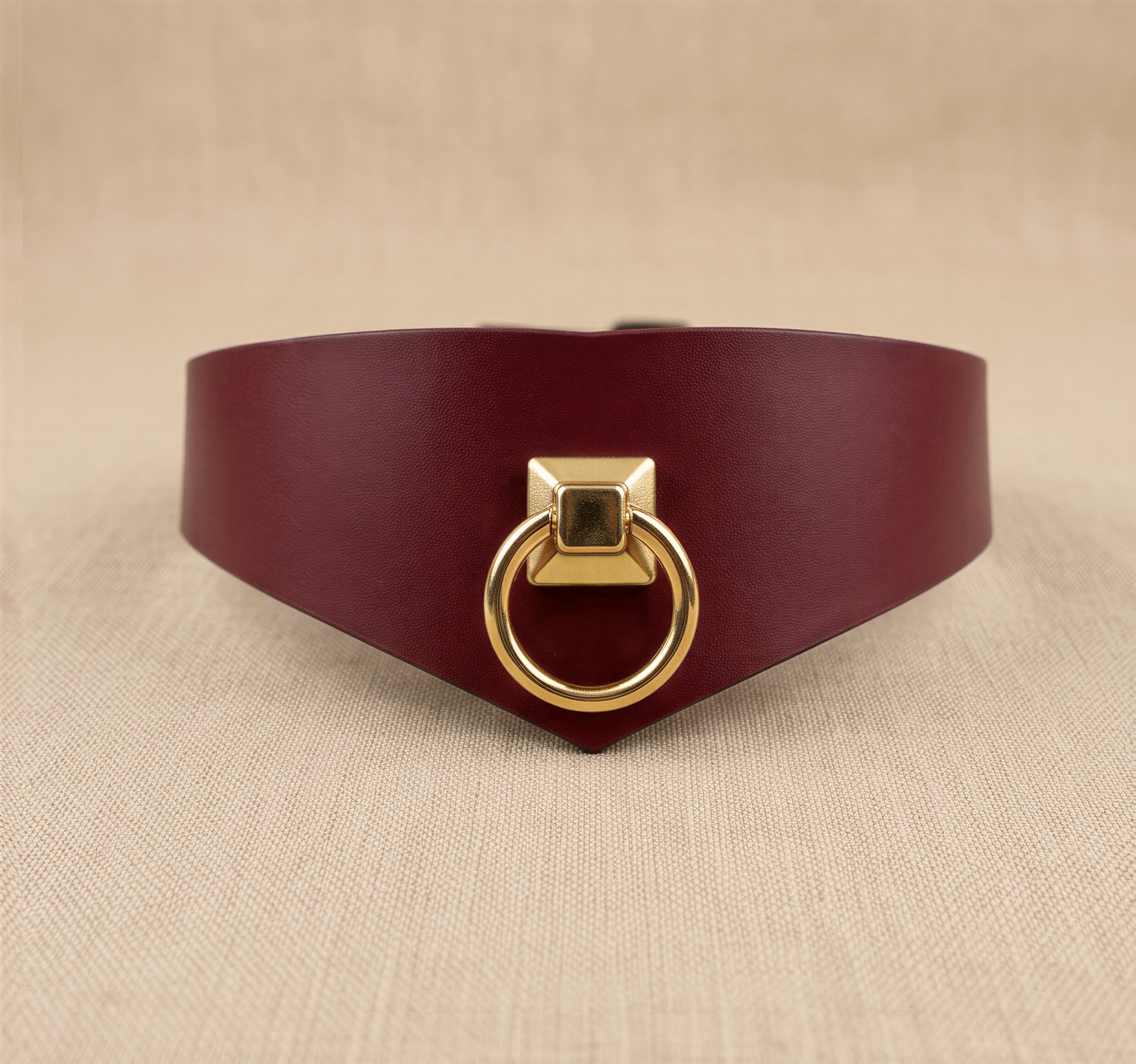 A burgundy leather choker necklace with a gold-colored metal ring on the front.