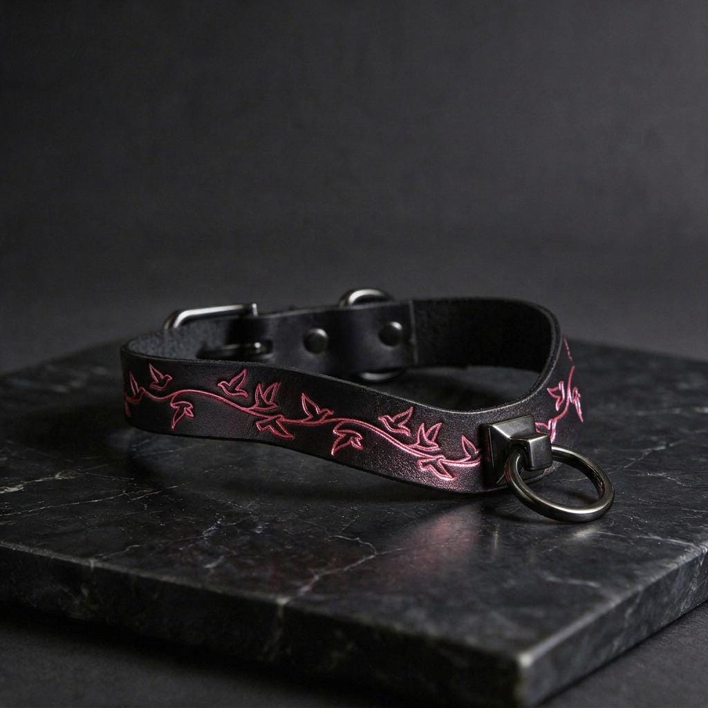 A black leather collar with a pink floral design on it, resting on a dark surface.