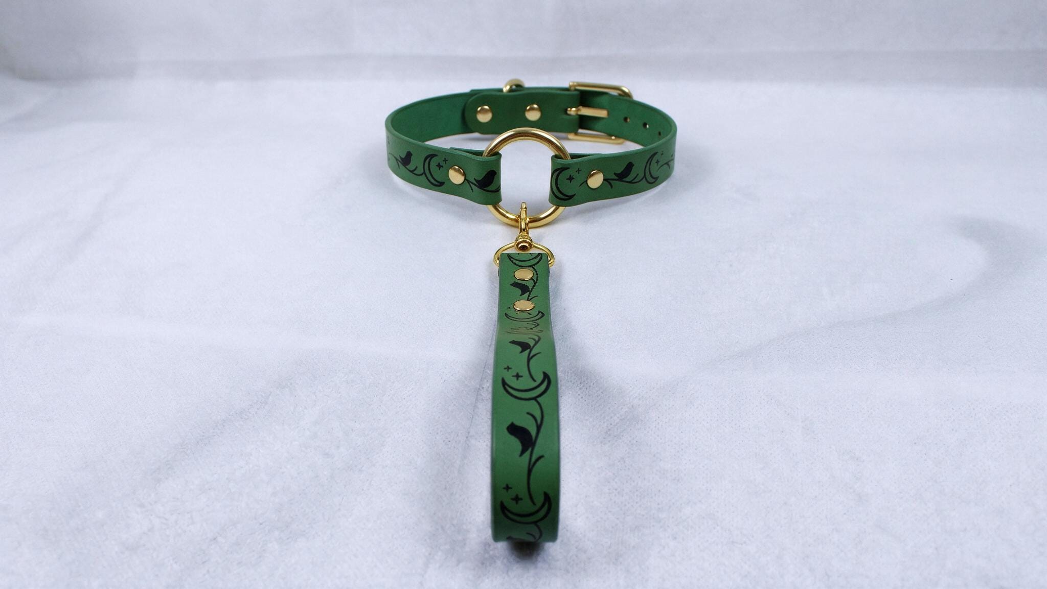 A green collar with a gold buckle and a green leash attached to it, resting on a white surface.