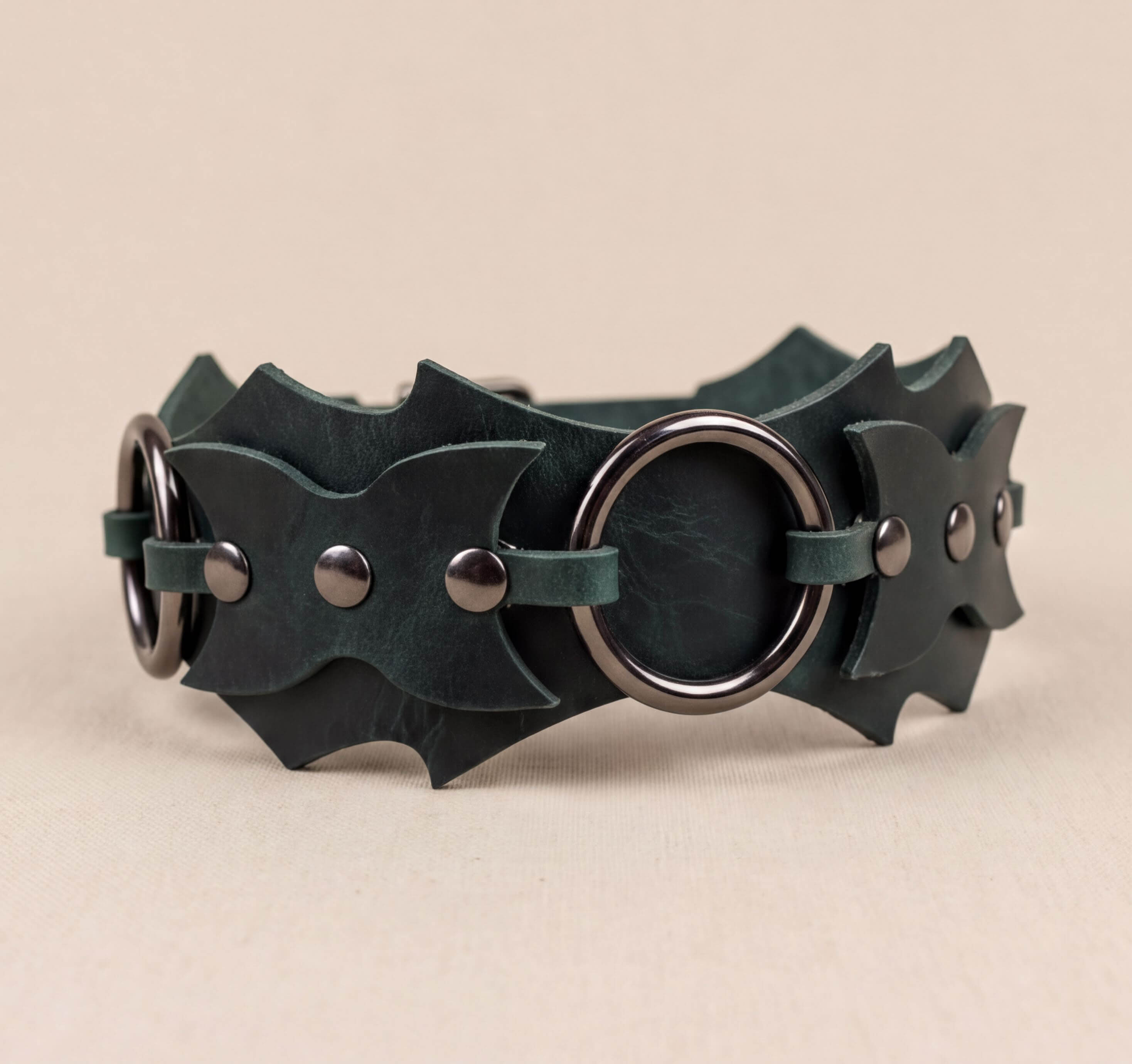 A dark green leather belt with metal rings and studs, featuring a unique and stylish design.