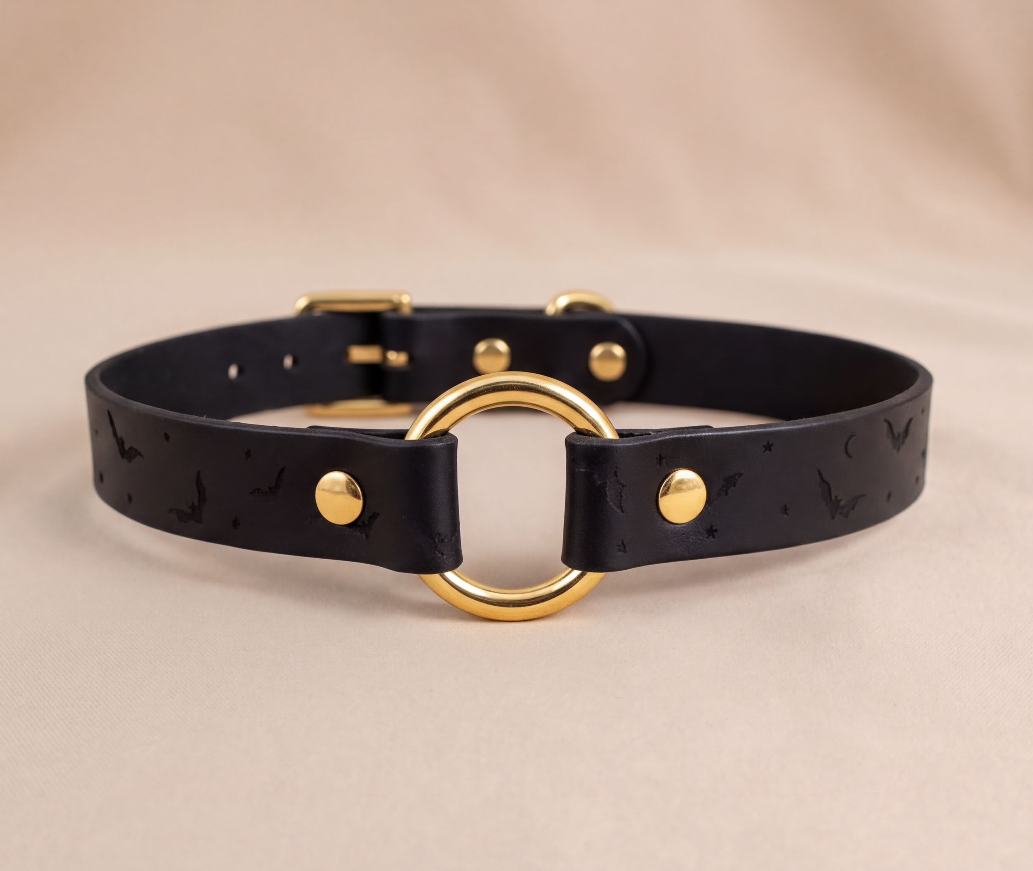 A black leather collar with a gold ring and a bat pattern design.