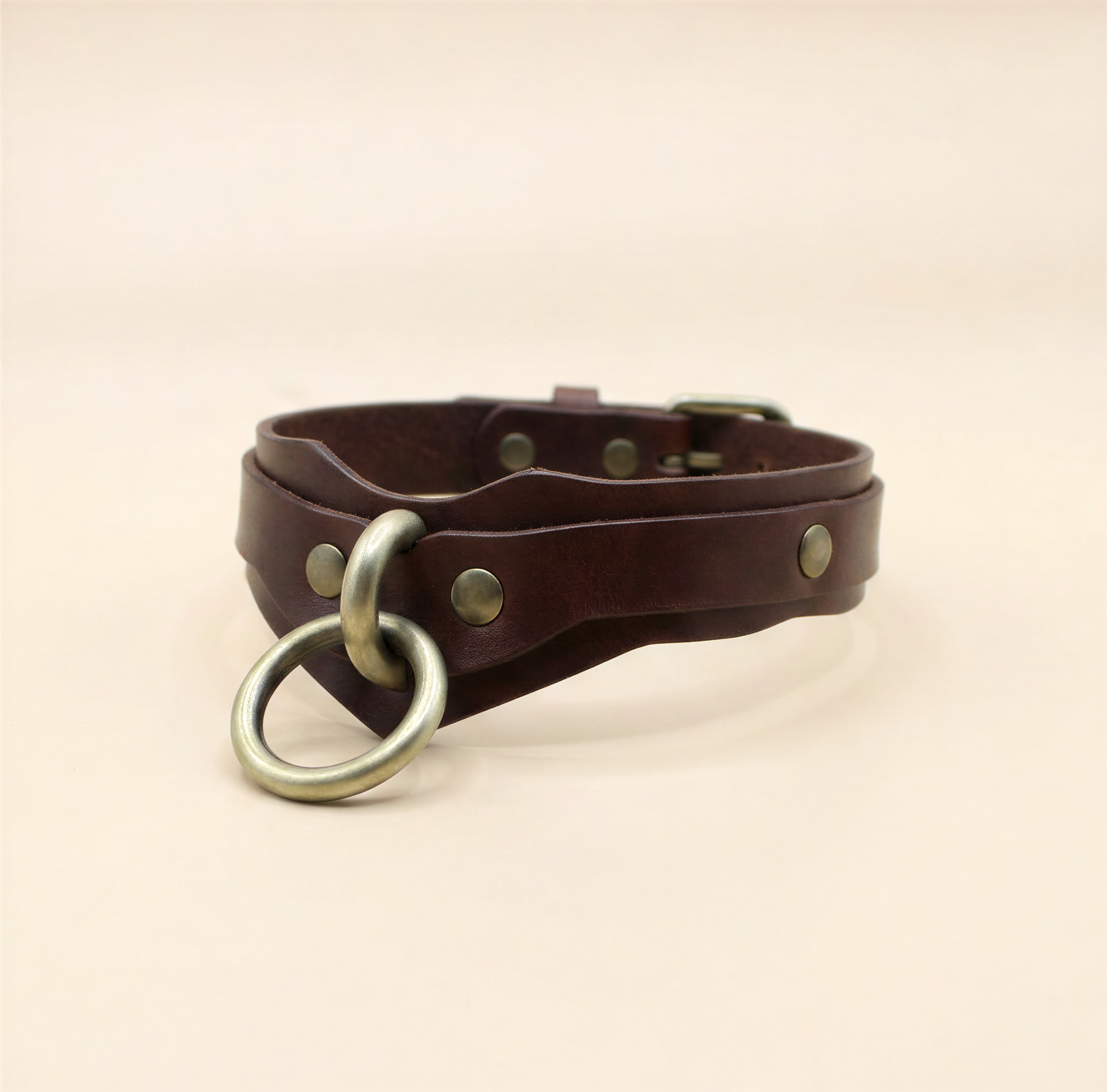 A brown leather choker collar with metal rings and buckles.