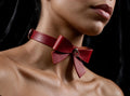 A close-up of a woman's neck and chest wearing a red leather choker with a bow detail.