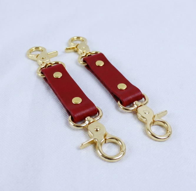 a pair of red leather straps with gold metal clasps and loops, placed on a white surface.